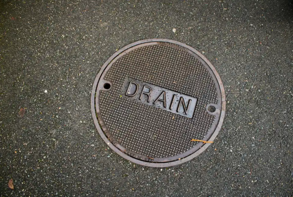 A round cast drain cover marked Drain set in tarmac