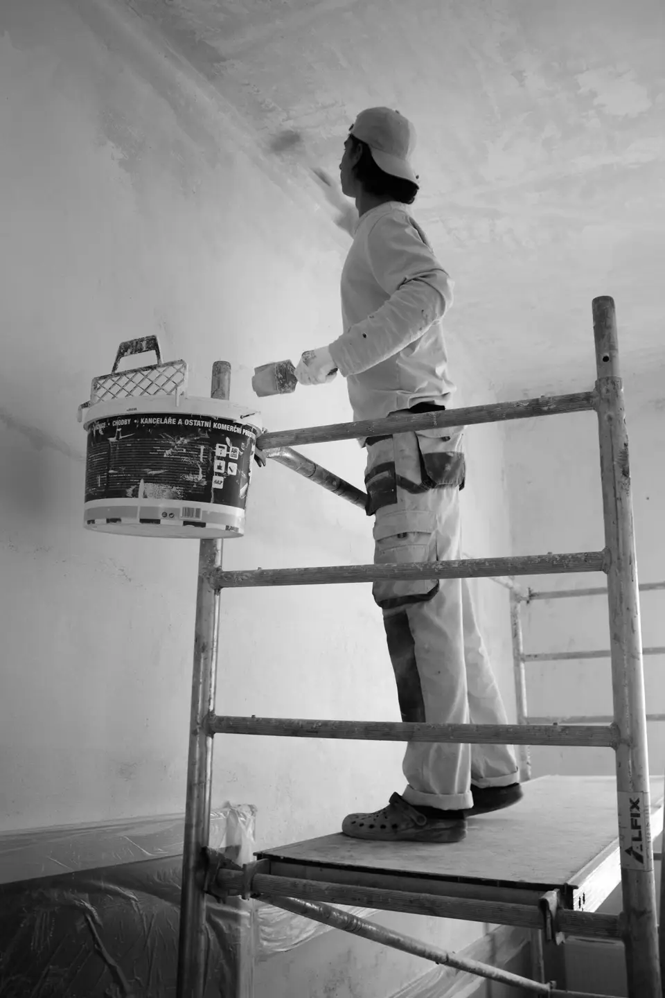 A decorator on a step ladder painting a wall white